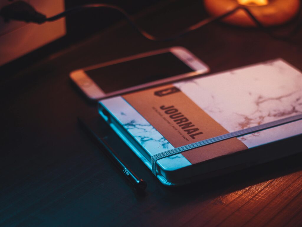 A calming workspace scene highlighting a journal, smartphone, and pen in warm lighting.