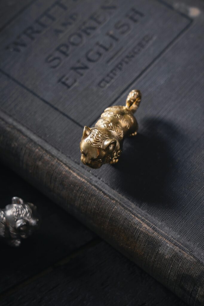 A gold cat figurine stands on a vintage book against a dark background, creating a mysterious atmosphere.