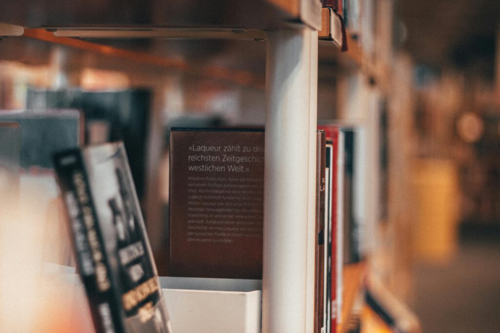 A close-up shot of books on a library bookshelf, featuring blurred background and warm tones.